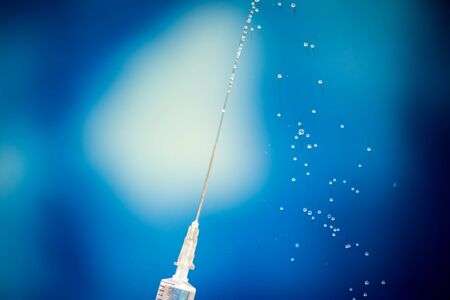 A syringe with flow of vaccine's liquid in front of blue background. Close-up shot. Medicine, science and healthcare conceptの写真素材