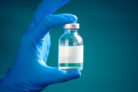 A doctor in blue gloves holding a bottle with vaccine. Close up shot. Medicine and healthcare conceptの写真素材