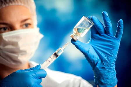 A doctor in medical gloves holding a bottle with vaccine and syringe before doing injection. Close up shot. Medicine and healthcare conceptの写真素材
