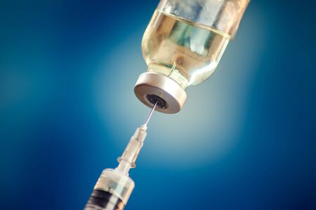A bottle with vaccine and syringe in front of blue background. Close up shot.  Medicine, science and healthcare conceptの写真素材