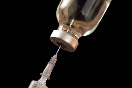 A bottle with vaccine and syringe in front of black background. Close up shot.の写真素材