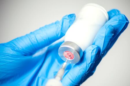 A doctor in medical gloves holding a bottle with vaccine and syringe before doing injection. Close up shot. Medicine and healthcare conceptの写真素材