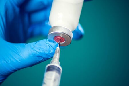 A doctor in medical gloves holding a bottle with vaccine and syringe before doing injection. Close up shot. Medicine and healthcare conceptの写真素材