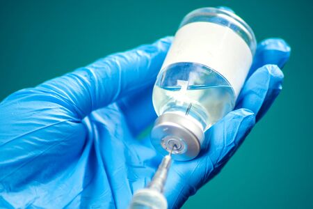 A doctor in medical gloves holding a bottle with vaccine and syringe before doing injection. Close up shot. Medicine and healthcare conceptの写真素材