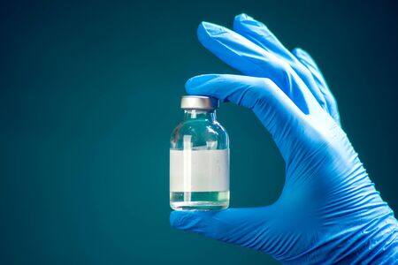 A doctor in blue gloves holding a bottle with vaccine. Close up shot. Medicine and healthcare conceptの写真素材
