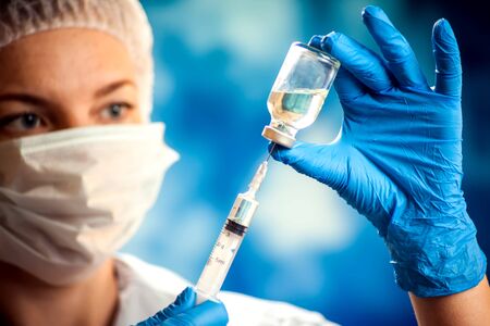 A doctor in medical gloves holding a bottle with vaccine and syringe before doing injection. Close up shot. Medicine and healthcare conceptの写真素材