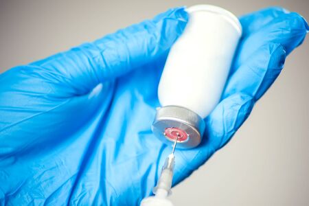 A doctor in medical gloves holding a bottle with vaccine and syringe before doing injection. Close up shot. Medicine and healthcare conceptの写真素材
