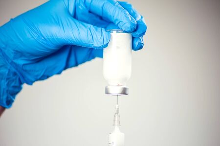 A doctor in medical gloves holding a bottle with vaccine and syringe before doing injection. Close up shot. Medicine and healthcare conceptの写真素材
