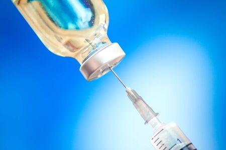 A bottle with vaccine and syringe in front of blue background. Close up shot.  Medicine, science and healthcare conceptの写真素材