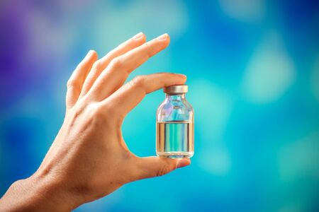 A doctor in blue gloves holding a bottle with vaccine. Close up shot. Medicine and healthcare conceptの写真素材