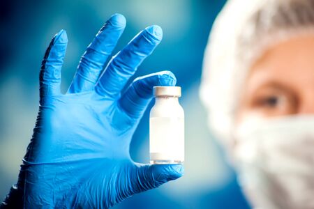 A doctor in blue gloves holding a bottle with vaccine. Close up shot. Medicine and healthcare conceptの写真素材