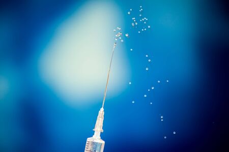A syringe with flow of vaccine's liquid in front of blue background. Close-up shot.の写真素材