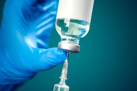 A doctor in medical gloves holding a bottle with vaccine and syringe before doing injection. Close up shot. Medicine and healthcare conceptの写真素材