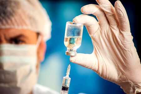 A doctor in medical gloves holding a bottle with vaccine and syringe before doing injection. Close up shot. Medicine, science and healthcare conceptの写真素材