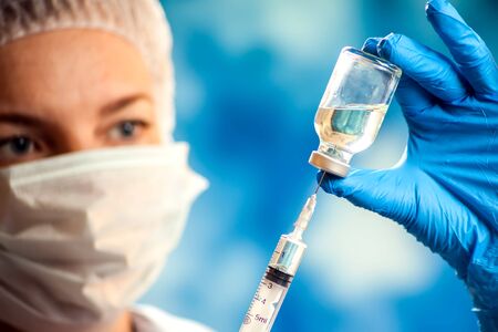 A doctor in medical gloves holding a bottle with vaccine and syringe before doing injection. Close up shot. Medicine and healthcare conceptの写真素材
