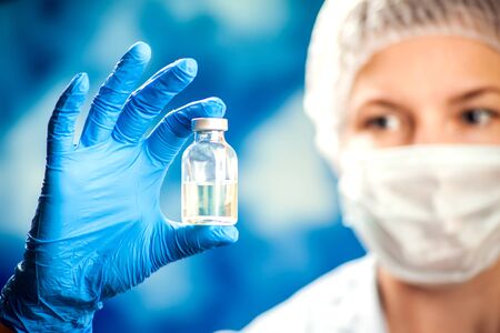 A doctor in blue gloves holding a bottle with vaccine. Close up shot. Medicine and healthcare conceptの写真素材