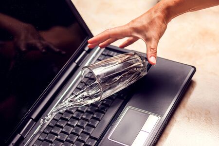 Spilling glass of water on the black laptop. Accident with technology
