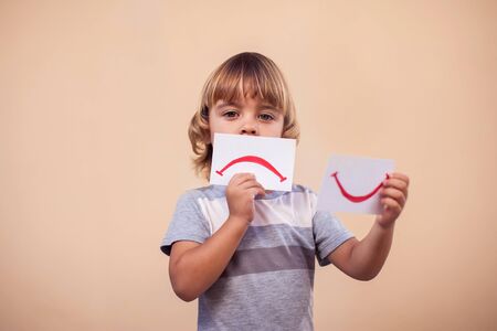 A portrait of kid boy holding cards with mood expression. Sad and good smile. Childhood and emotion conceptの写真素材