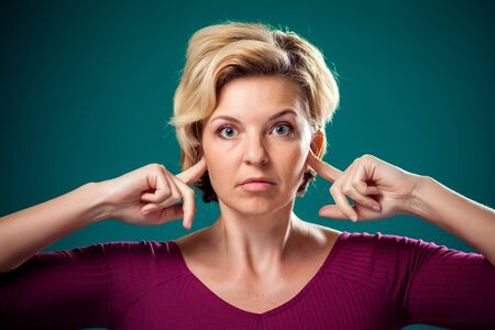 A portrait of woman with short blond hair closing her ears. People,lifestyle and emotions concept