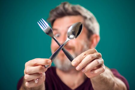 A portrait of bearded hungry man holding spoon and fork in hands. People and food conceptの写真素材