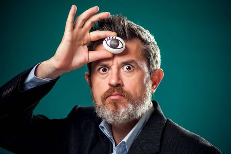A portrait of bearded man in suit holding egg with drawing eye near forehead. Third eye conceptの写真素材