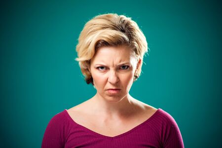 Angry woman with short blond hair in front of green background . People and emotions conceptの写真素材