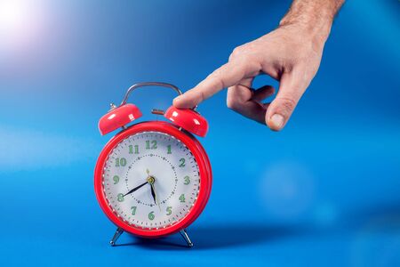 Red alarm clock on the color background. A hand of person switching off an alarm clock in the...