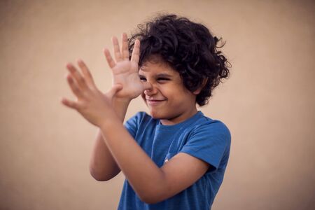 A portrait of happy kid boy with curly hair showing tease gesture. Children and emotions conceptの写真素材