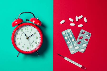 Red alarm clock, pills and thermometer on the color background. Healthcare and medicine conceptの写真素材