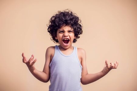 A portrait of angry kid boy with curly hair showing aggresion. Children and emotions conceptの写真素材