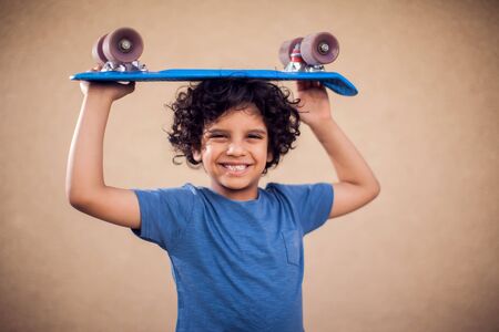 A portrait of happy kid boy with curly hair holding skateboard. Children,leisure and lifestyle...