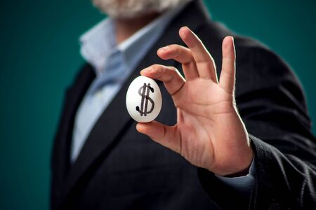 A portrait of bearded man in suit holding white egg with drawing dollar sign. Business and finance conceptの写真素材