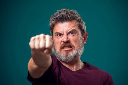 A portrait of bearded angry man in red t-shirt showing fist at camera. People and emotions conceptの写真素材