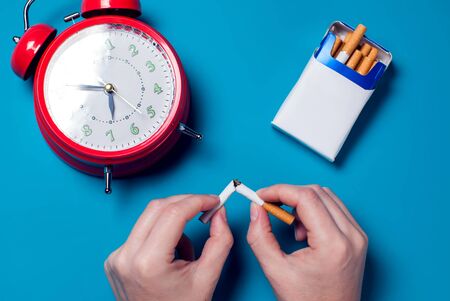 Red alarm clock and hand of woman breakening cigarettes on color background. Healthcare and stop smoking conceptの写真素材