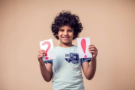 A portrait of kid boy holding cards with question mark and exclamation point. Childhood and education conceptの写真素材