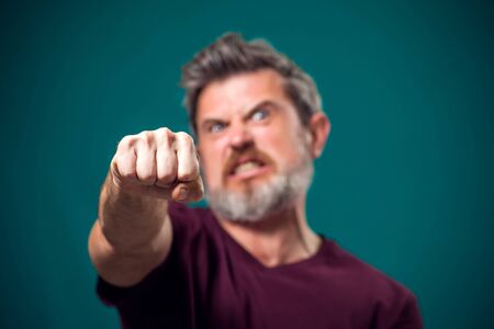 A portrait of bearded angry man in red t-shirt showing fist at camera. People and emotions conceptの写真素材