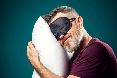 Man in red t-shirt and sleep mask on head holding white pillow. Lifestyle and bed time conceptの写真素材