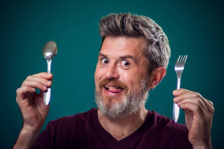 A portrait of bearded hungry man holding spoon and fork in hands. People and food conceptの写真素材