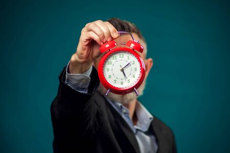 Bearded businessman in suit holding red alarm clock. Time management concept