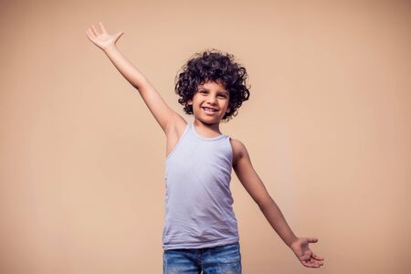 A portrait of smiling kid boy with curly hair showing embrace gesture at camera. Children and emotions conceptの写真素材