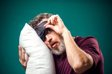 Man in red t-shirt and sleep mask on head holding white pillow. Lifestyle and bed time conceptの写真素材