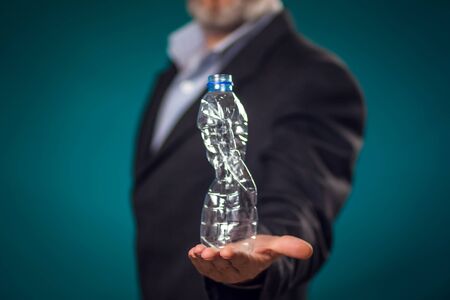 Man in suit holding damaged plastic bottle in hand. Close up. Business, environment protection and ecology concept の写真素材