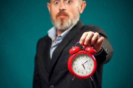 Surprised bearded businessman in suit holding red alarm clock. Time management conceptの写真素材