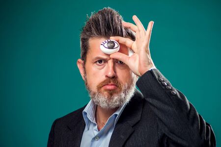 A portrait of bearded man in suit holding egg with drawing eye near forehead. Third eye conceptの写真素材