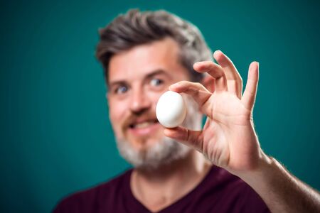A portrait of bearded man holding white egg in hand. People and food conceptの写真素材
