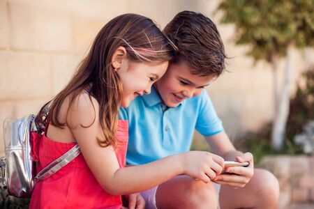 Two kids boy and girl holding smartphone and play games outdoor. Children and gadget addiction...