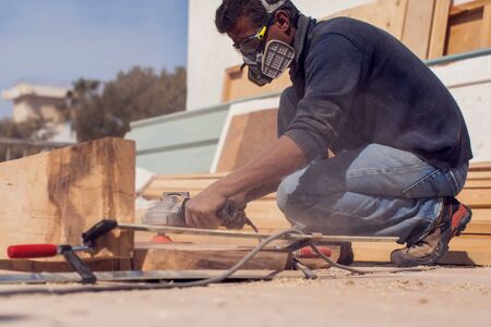 A handyman in mask polishing wooden plank outdoor. の写真素材