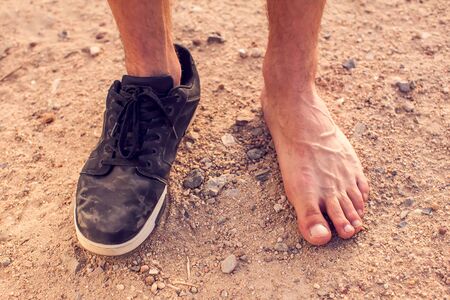 Men's feet with one dirty black shoe outdoor. Poverty conceptの写真素材