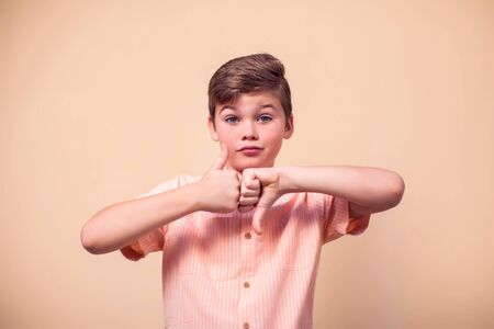 A portrait of cute kid boy showing thumb up and down gesture. Children and emotions conceptの写真素材