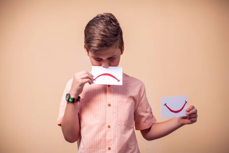 A portrait of kid boy holding positive and negative smile cards. Children and emotions conceptの写真素材